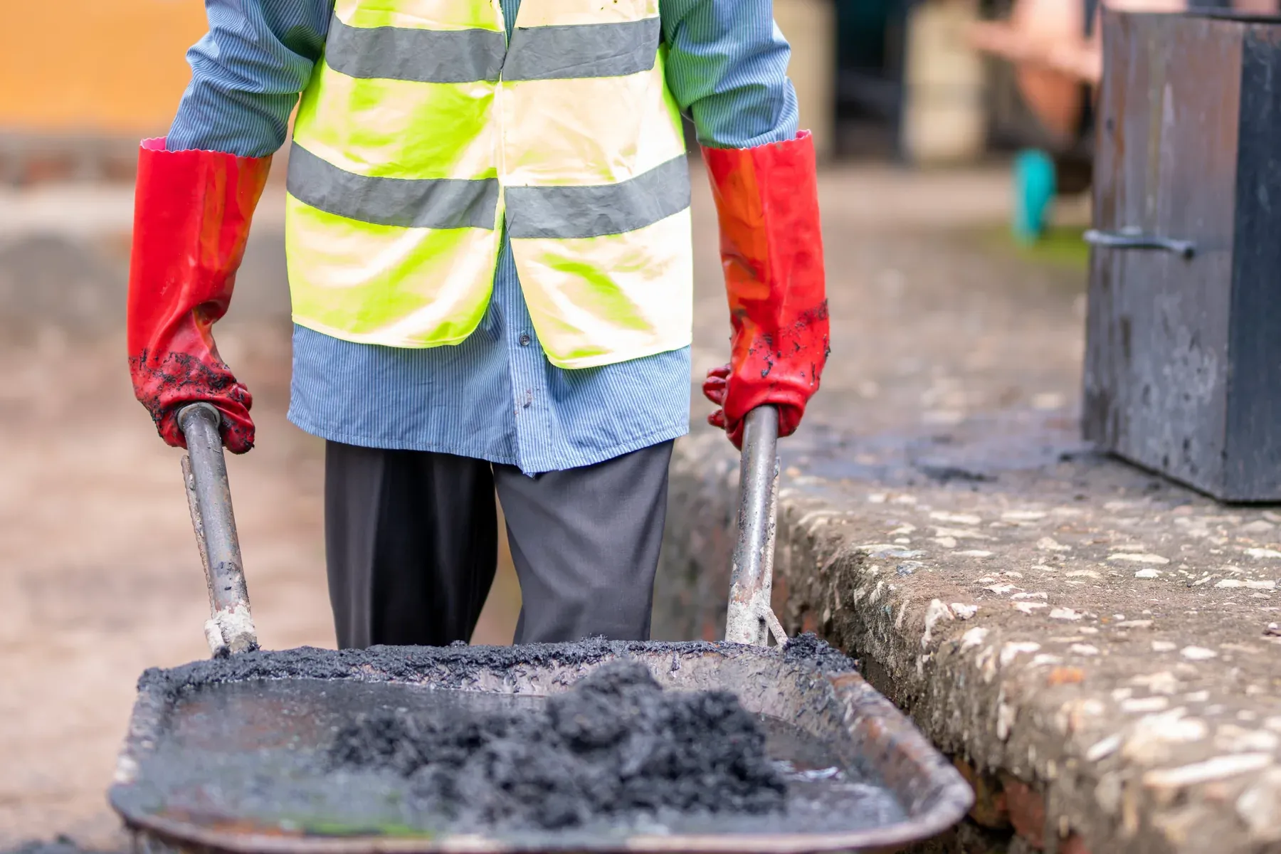 A plant worker in protective equipment moving a barrow of biochar