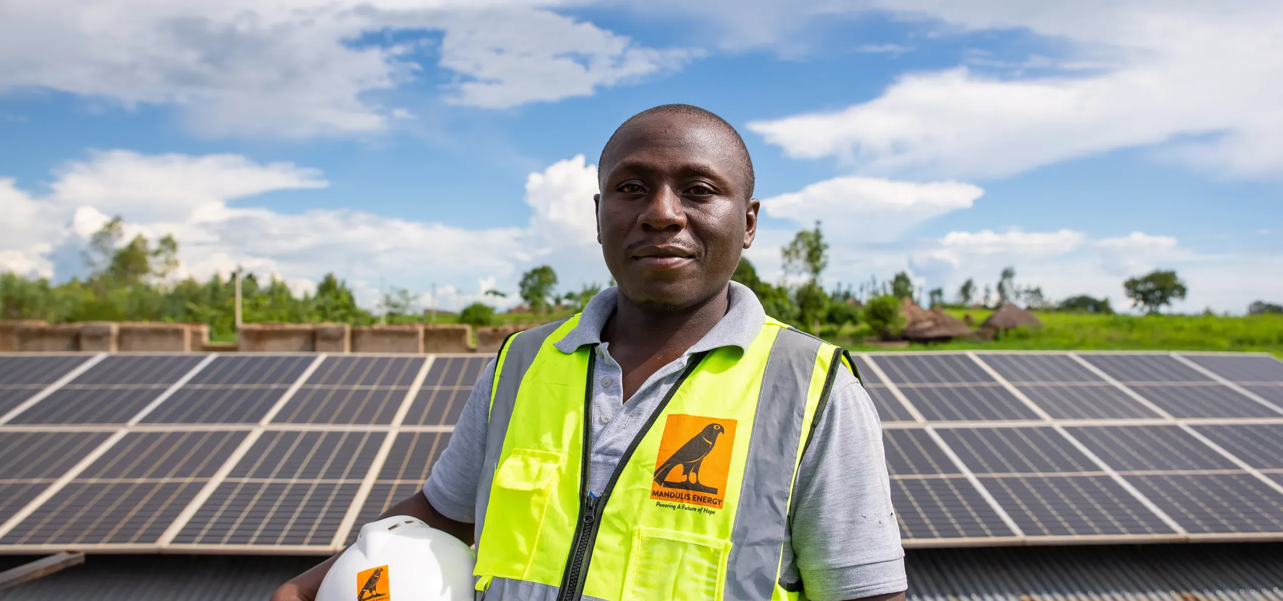A Mandulis Energy technician holding his helmet in front of the solar array at Got Ngur